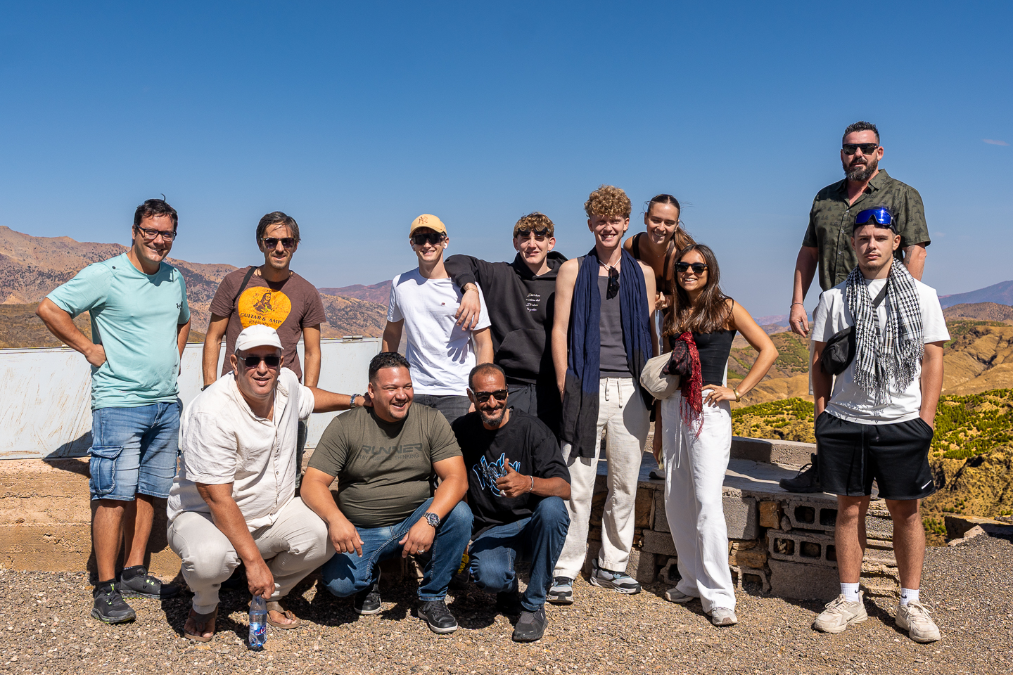 Group of people posing at a viewpoint in Tizi n’Tichka, Morocco, with rugged mountains beneath a clear blue sky.