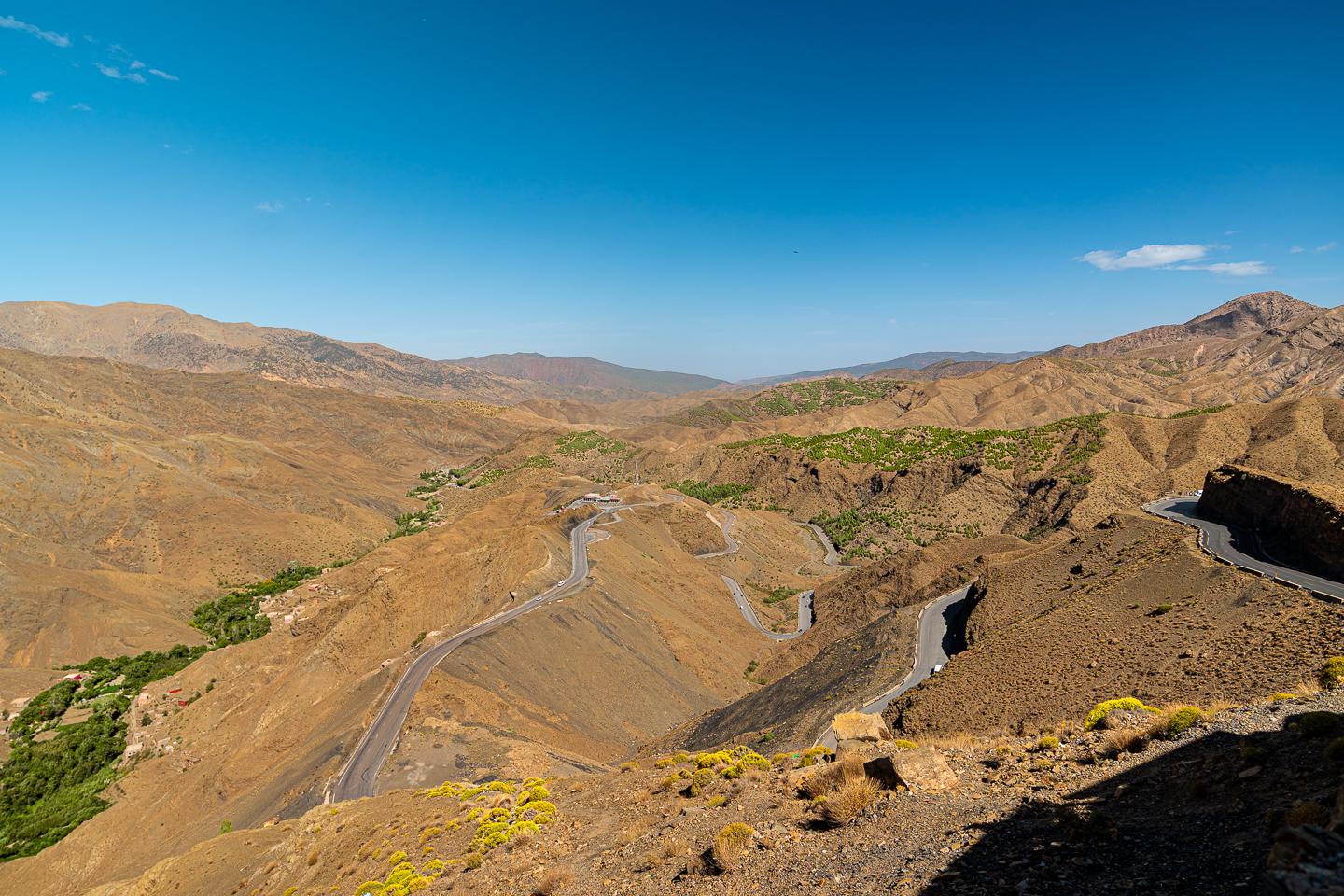 Winding road through the rugged mountains of Tizi n’Tichka, Morocco, with hairpin bends and patches of greenery beneath a bright blue sky.