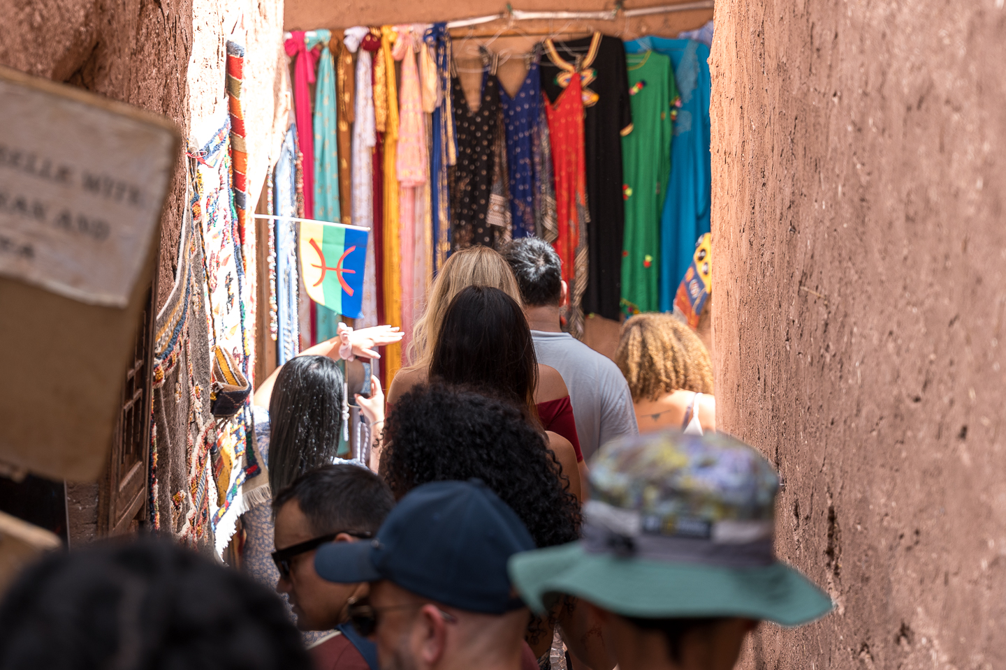Wooden entrance and direction signs at Ait Ben Haddou, Morocco, surrounded by earthen buildings and palm trees.